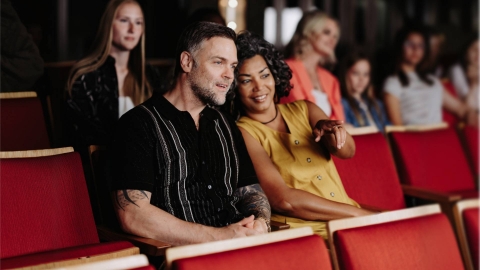 Deux personnes assises sur des fauteuils de th&eacute;&acirc;tre rouges, en train d'assister &agrave; un spectacle. 