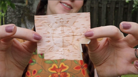 An Indigenous woman holds up her birchbark biting art.
